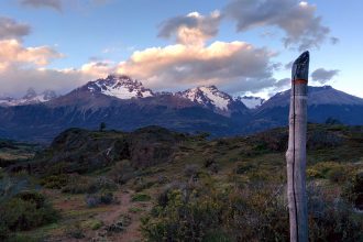 In the nature during a sunset, the Cerro Castillo in the background. There is a signpost that shows the way.