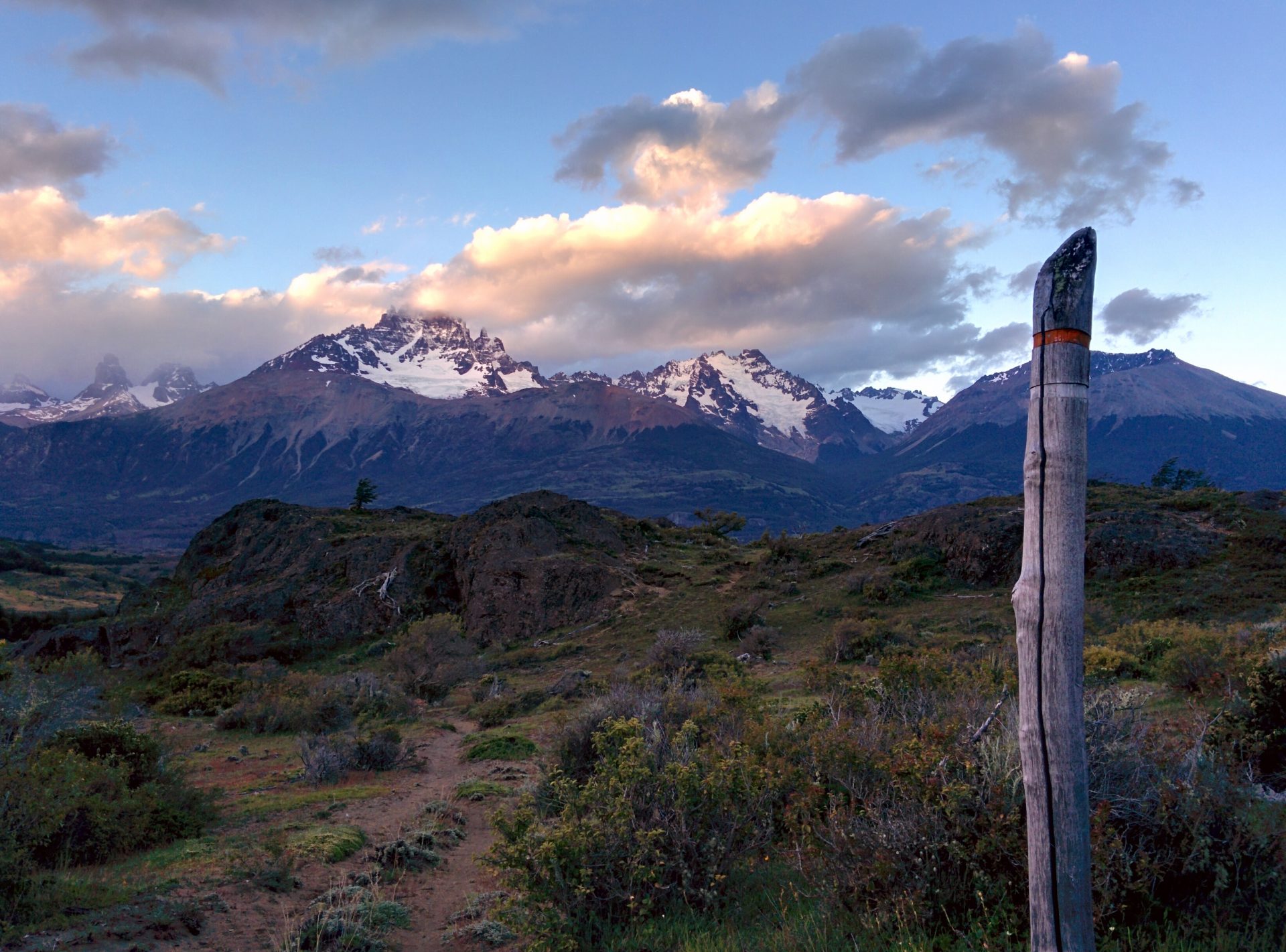In the nature during a sunset, the Cerro Castillo in the background. There is a signpost that shows the way.